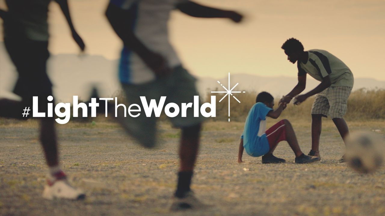 Αγόρι βοηθά ένα άλλο αγόρι να σηκωθεί, αφού έχει πέσει στο ποδόσφαιρο από το βίντεο Φωτίστε τον Κόσμο